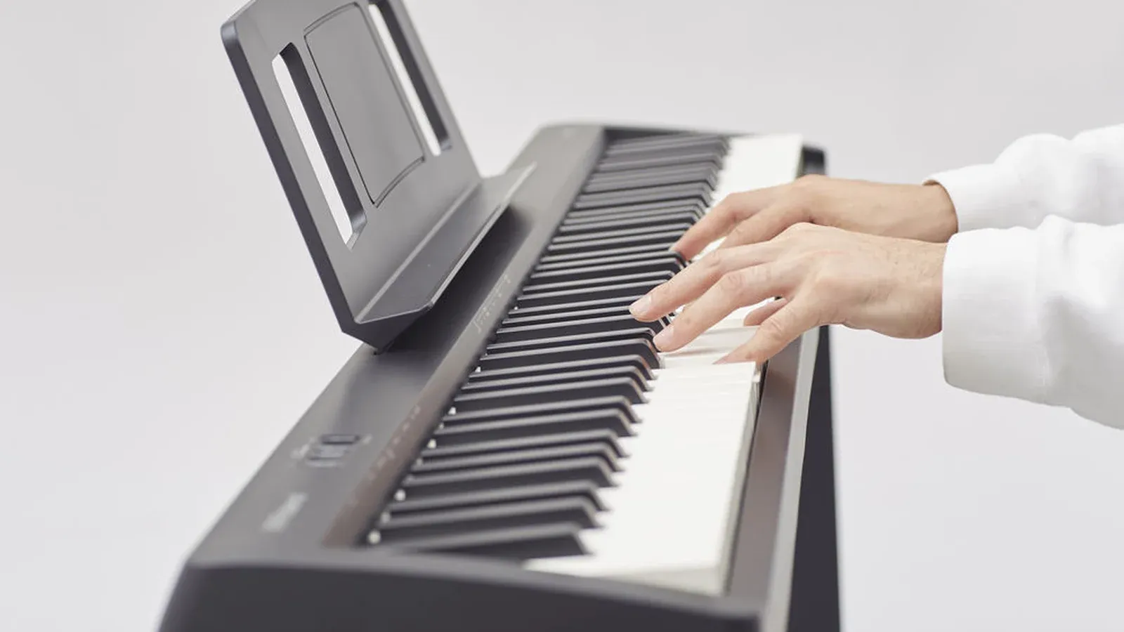 Hands playing the Roland FP-10 digital piano, with the music rest up and the matte black keys in view